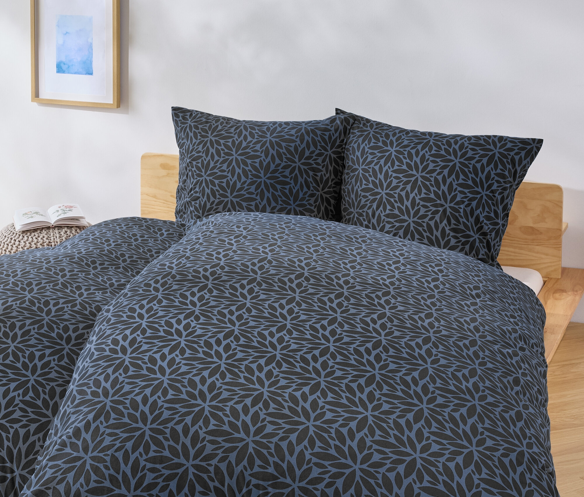 Łóżko z niebiesko-czarną pościelą w kwiaty i dwiema poduszkami.