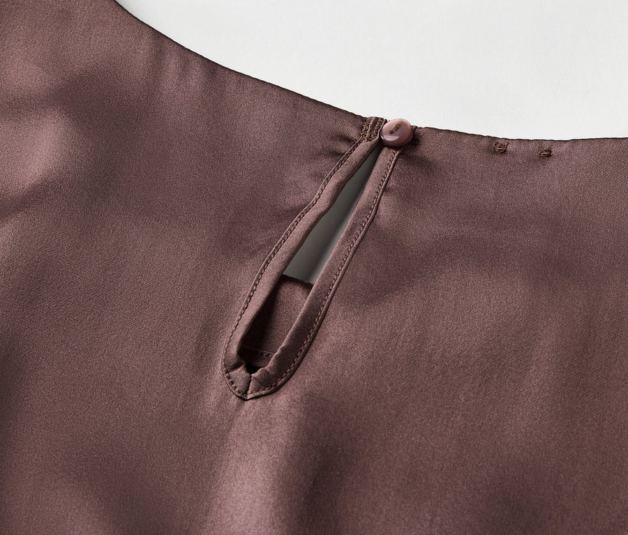 Szczegół brązowej satynowej bluzki z dziurką od klucza i zapięciem na guzik z tyłu szyi.