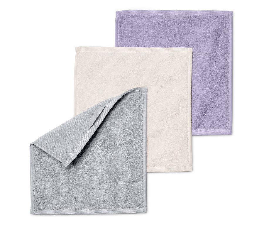 Trzy ręczniki złożone jeden na drugim: szary, kremowy i fioletowy.