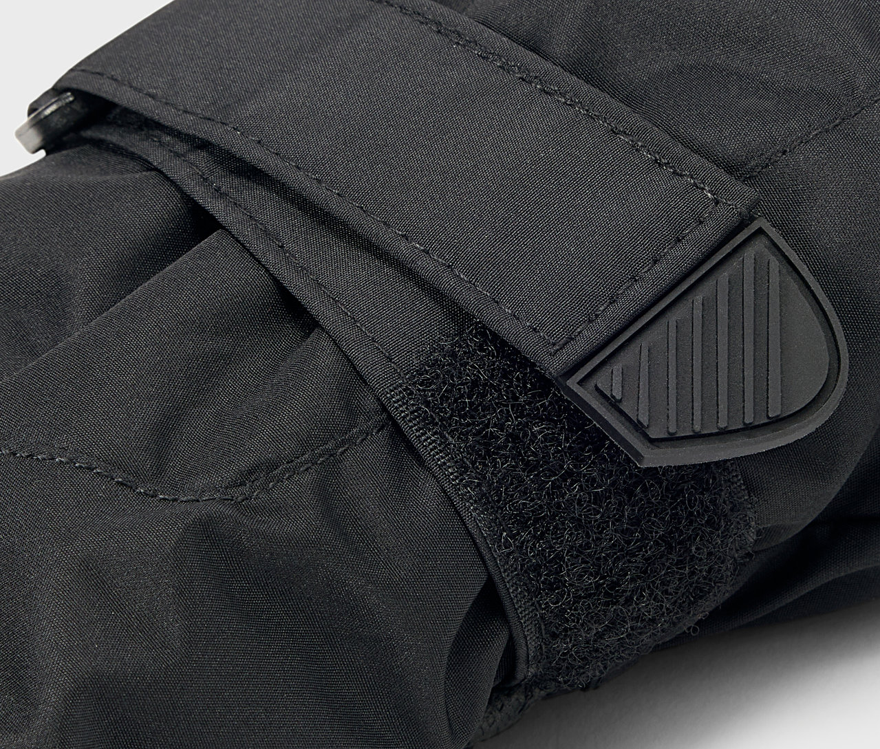 Szczegół czarnej rękawicy z zapięciem na rzep i gumowym wykończeniem paska.