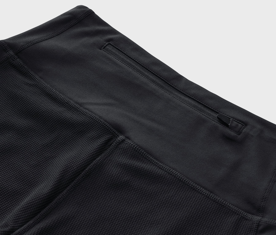 Szczegółowe ujęcie czarnych legginsów trekkingowych o długości 3/4 z kieszenią na zamek błyskawiczny w pasie.