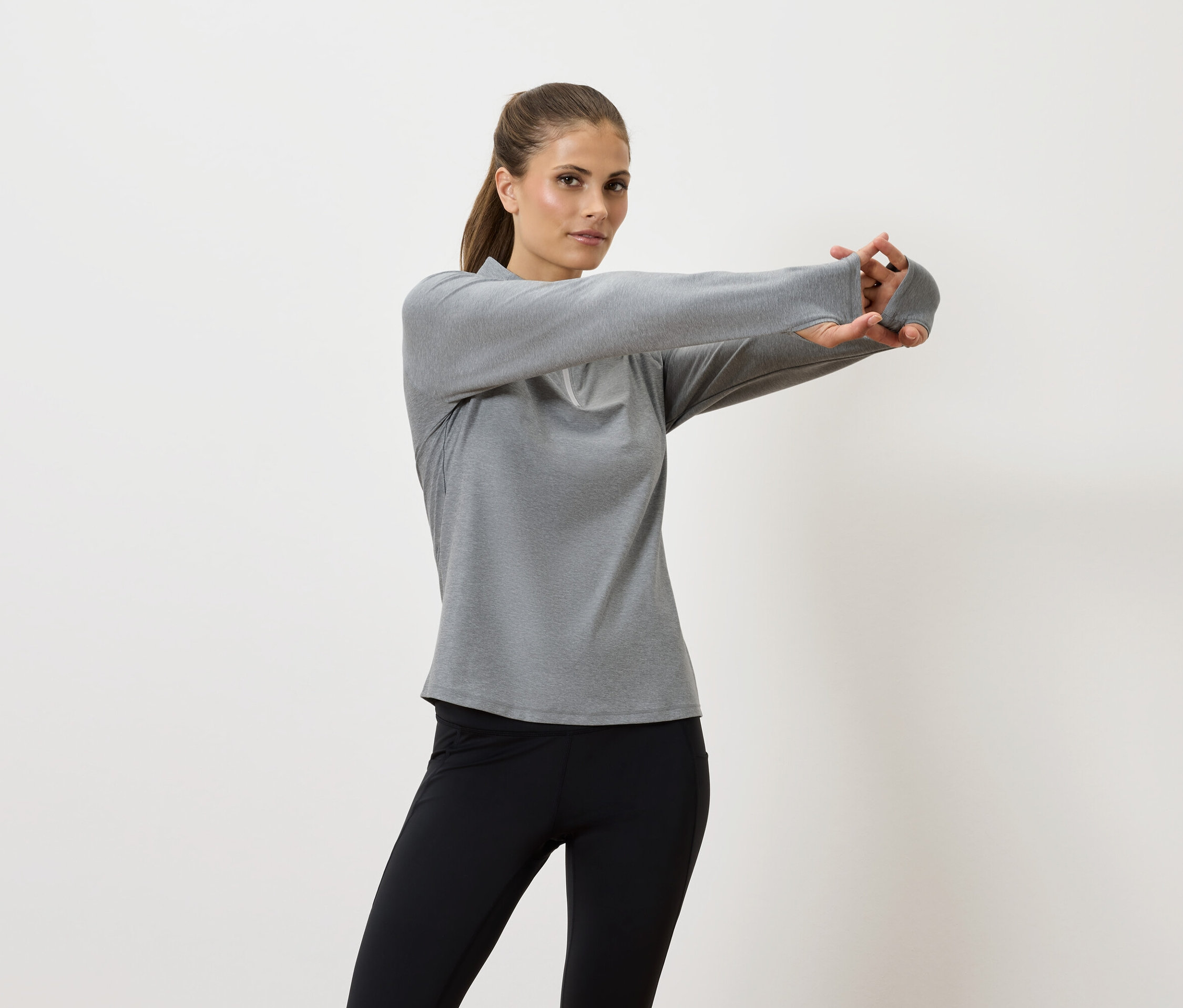 Kobieta rozciąga ręce w szarej koszuli z długim rękawem i czarnych legginsach.