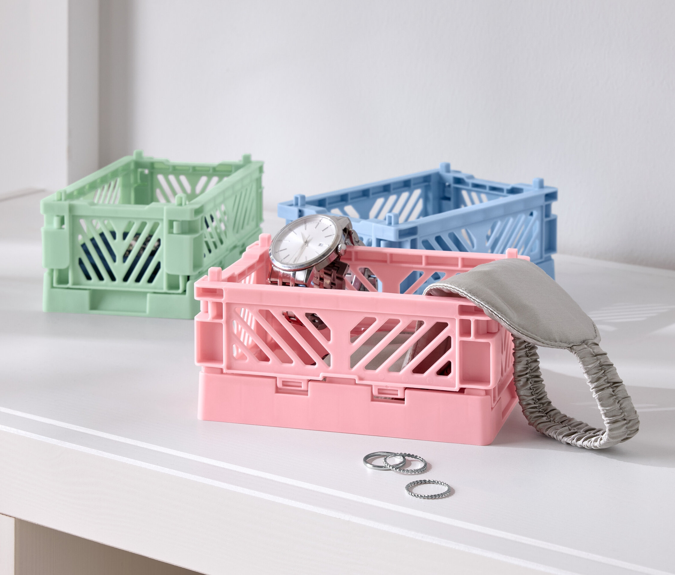 Trzy kolorowe składane pudełka na stole, jedno różowe z zegarkiem, jedno niebieskie i jedno zielone.