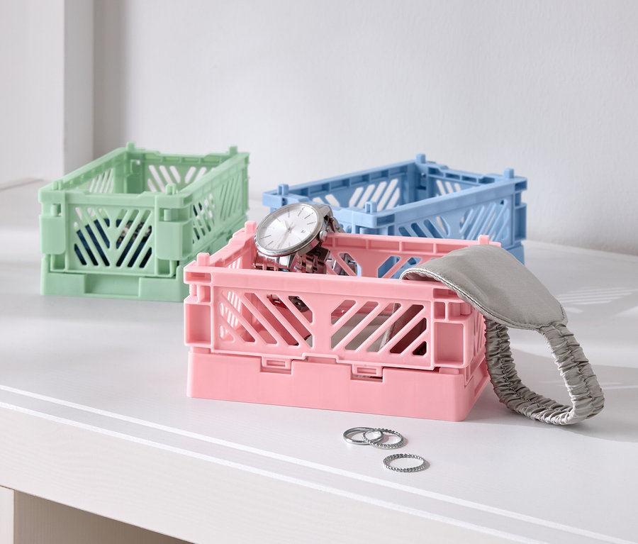 Trzy kolorowe składane pudełka na stole, jedno różowe z zegarkiem, jedno niebieskie i jedno zielone.