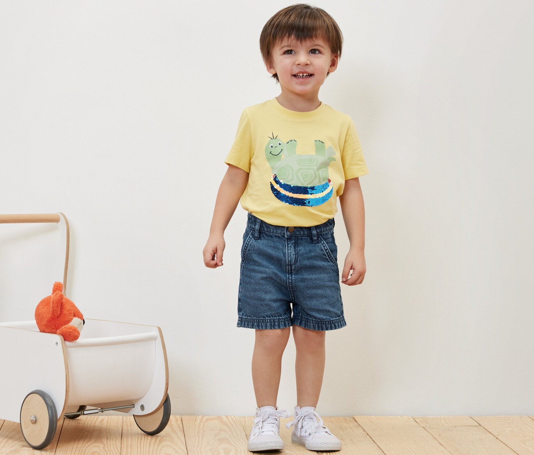 Chłopiec stoi obok szortów dżinsowych i zabawki w chodziku.