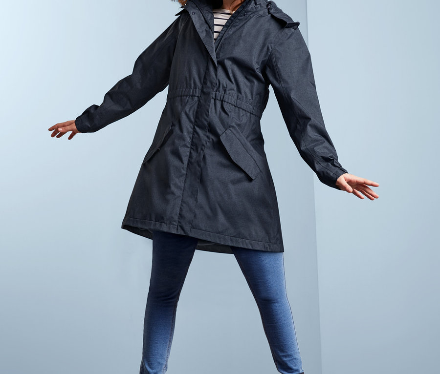 Uśmiechnięta dziewczyna pozuje w dziewczęcej kurtce przeciwdeszczowej stylizowanej na dżins, niebieskich dżinsach i butach.