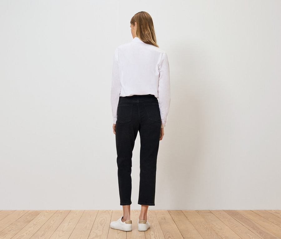 Z tyłu widać kobietę w białej koszuli, czarnych spodniach i białych butach.