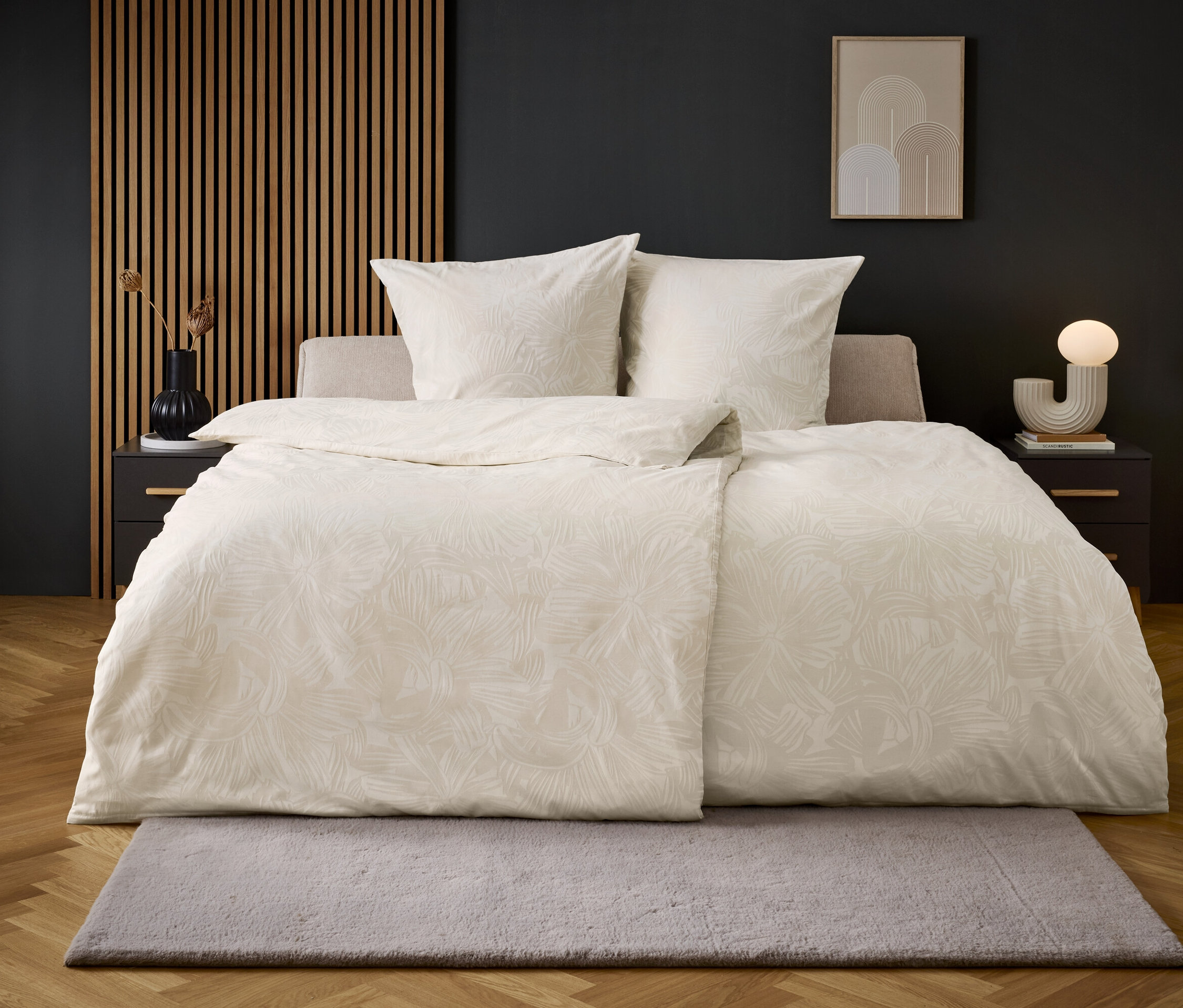 Beżowe łóżko z białą pościelą na podłodze z szarym dywanem.