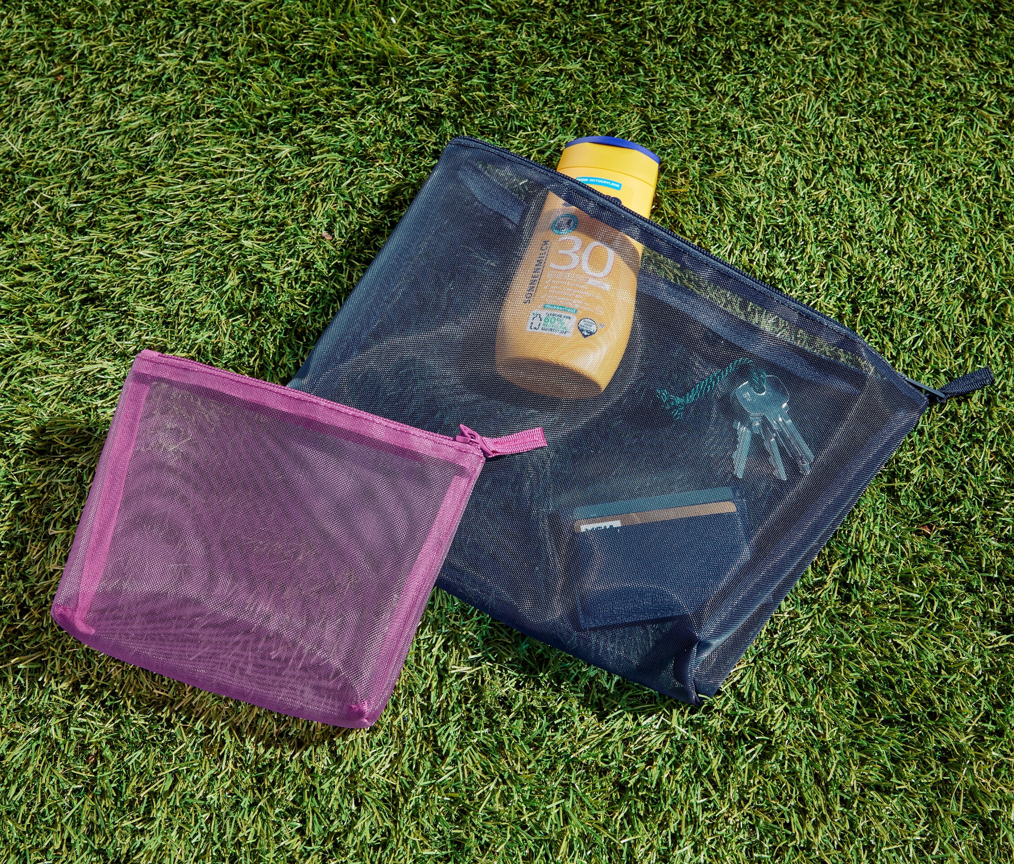 Dwie Torebki do przechowywania leżą na trawie. W jednej z nich jest krem do opalania, klucze i karta.