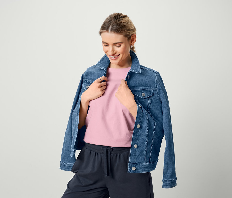 Kobieta ma na sobie kurtkę dżinsową, różową koszulkę i dresowe szorty.
