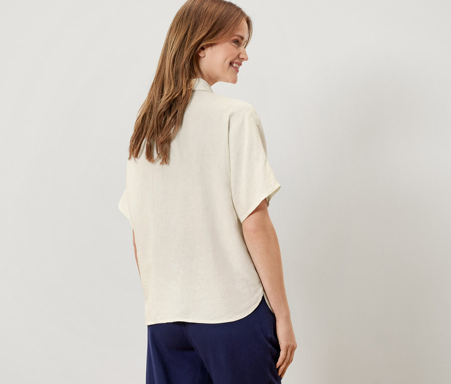 Kobieta stoi tyłem, ubrana w kremową lnianą bluzkę.