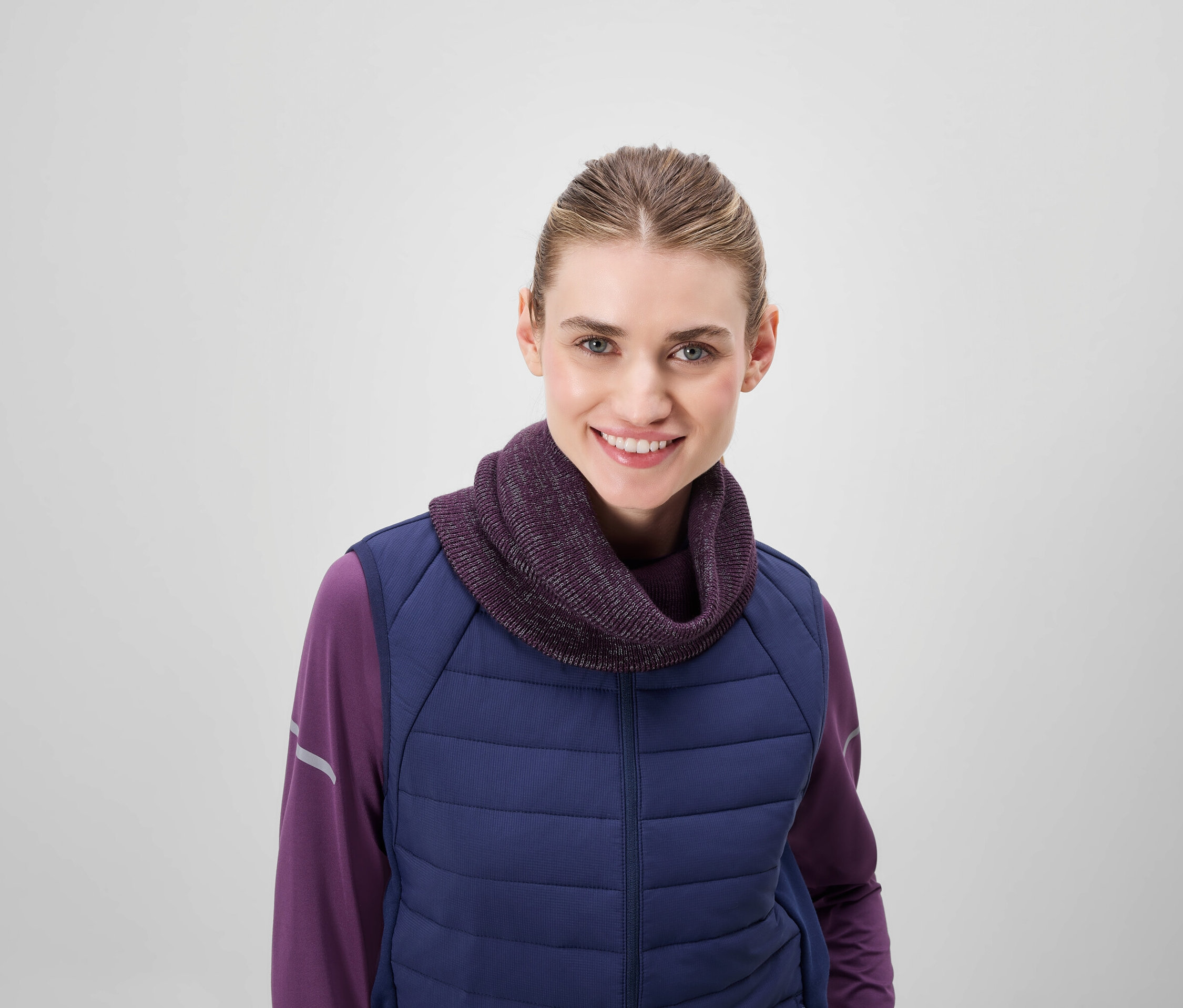 Uśmiechnięta kobieta ma na sobie fioletowy golf i niebieską pikowaną kamizelkę.