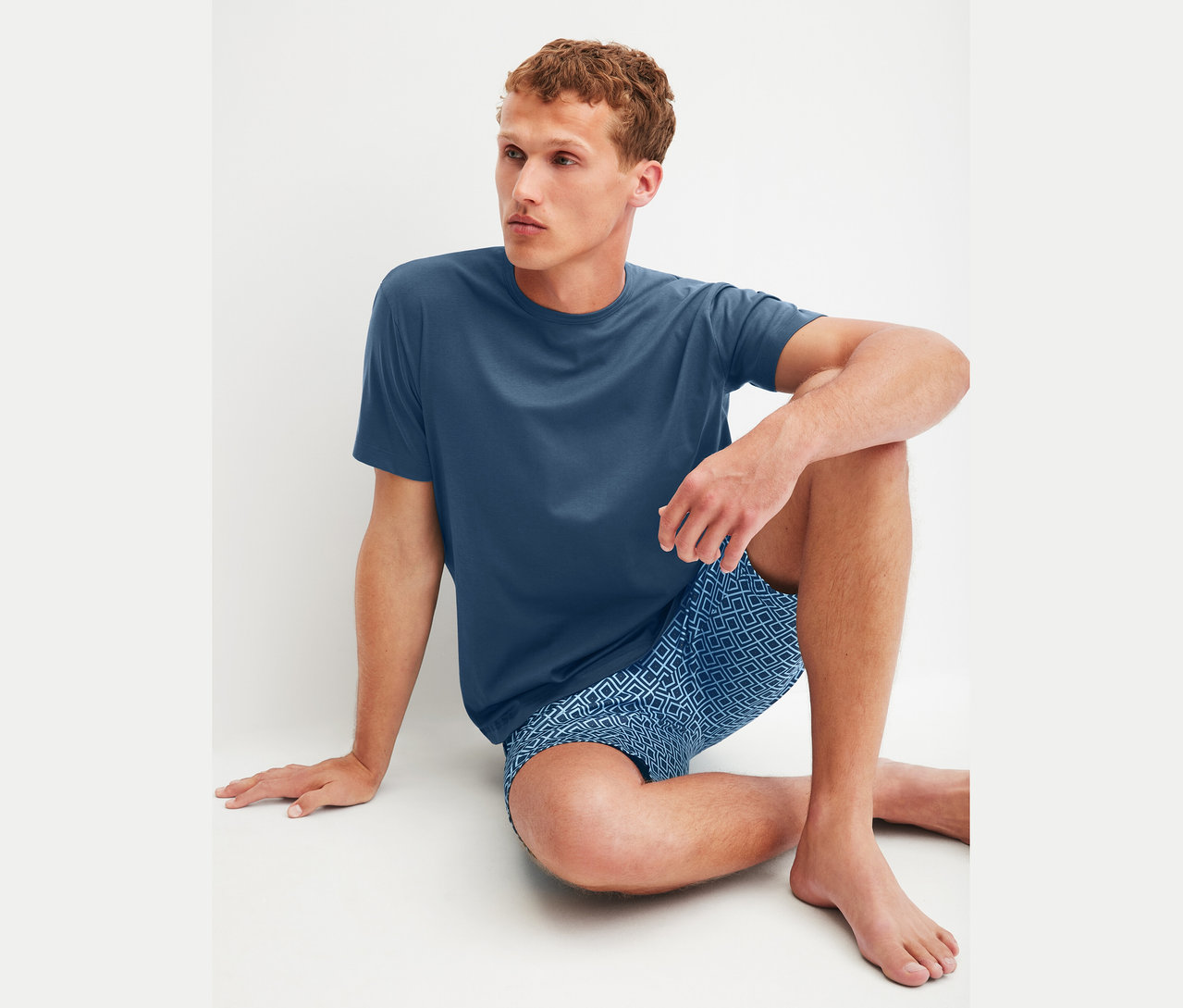 Mężczyzna siedzi na podłodze, ubrany w niebieski T-shirt i niebieskie szorty w geometryczny wzór.