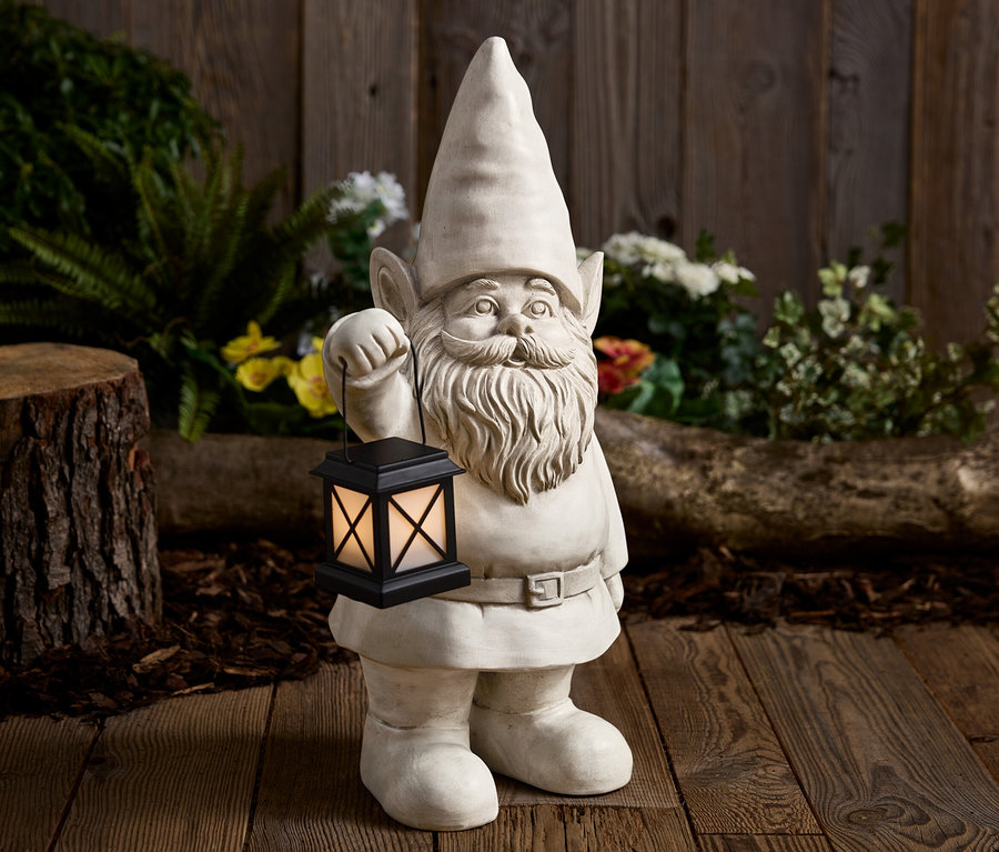 Kamienny krasnal ogrodowy trzyma czarną latarnię na tle drewnianego tła.