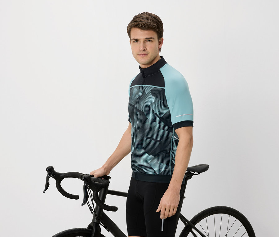 Mężczyzna w koszulce rowerowej z niebiesko-zielonymi rękawami trzyma czarny rower.