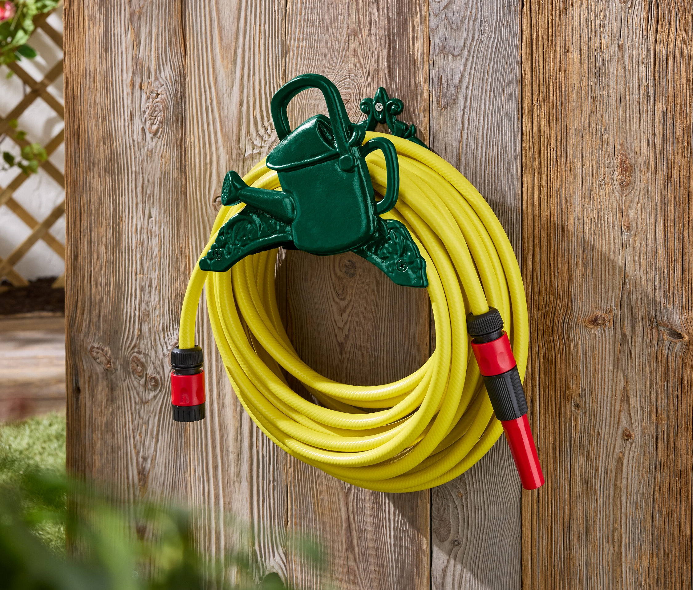 Żółty wąż ogrodowy przymocowany do zielonego uchwytu w kształcie konewki na drewnianej ścianie.