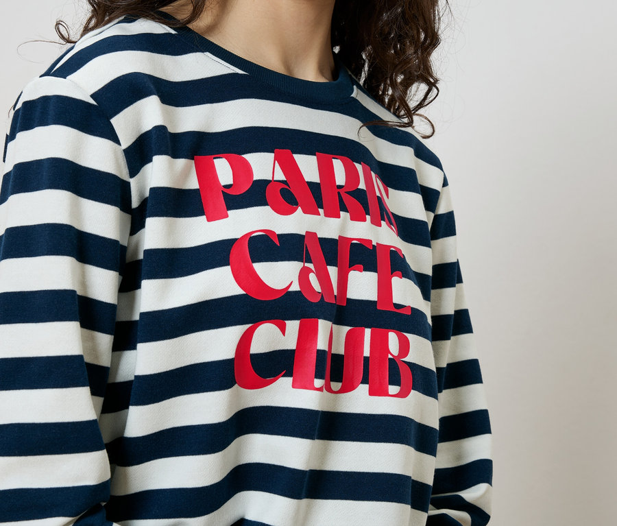 Kobieta ma na sobie bluzę w niebiesko-białe paski z czerwonym napisem "Paris Cafe Club".