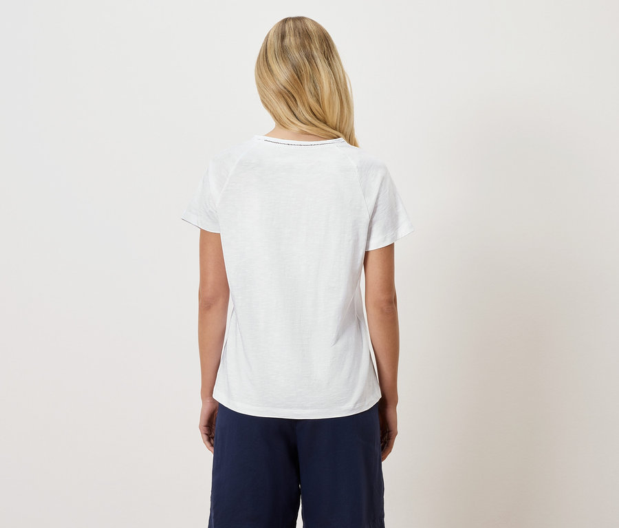 Widok z tyłu blondwłosej kobiety w białym T-shircie i ciemnoniebieskich spodniach.