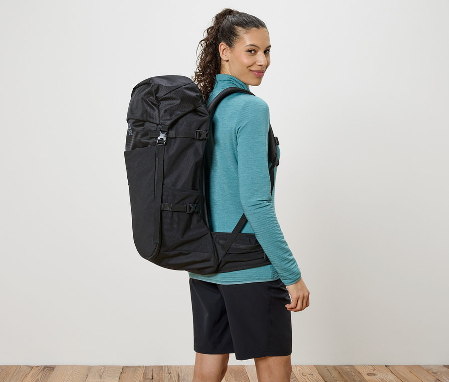 Kobieta z czarnym plecakiem przewieszonym przez ramiona, spogląda przez ramię.