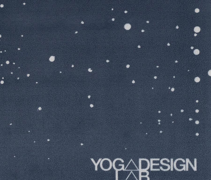 Zbliżenie na ciemnoniebieską matę do jogi z białymi kropkami i logo Yoga Design Lab.