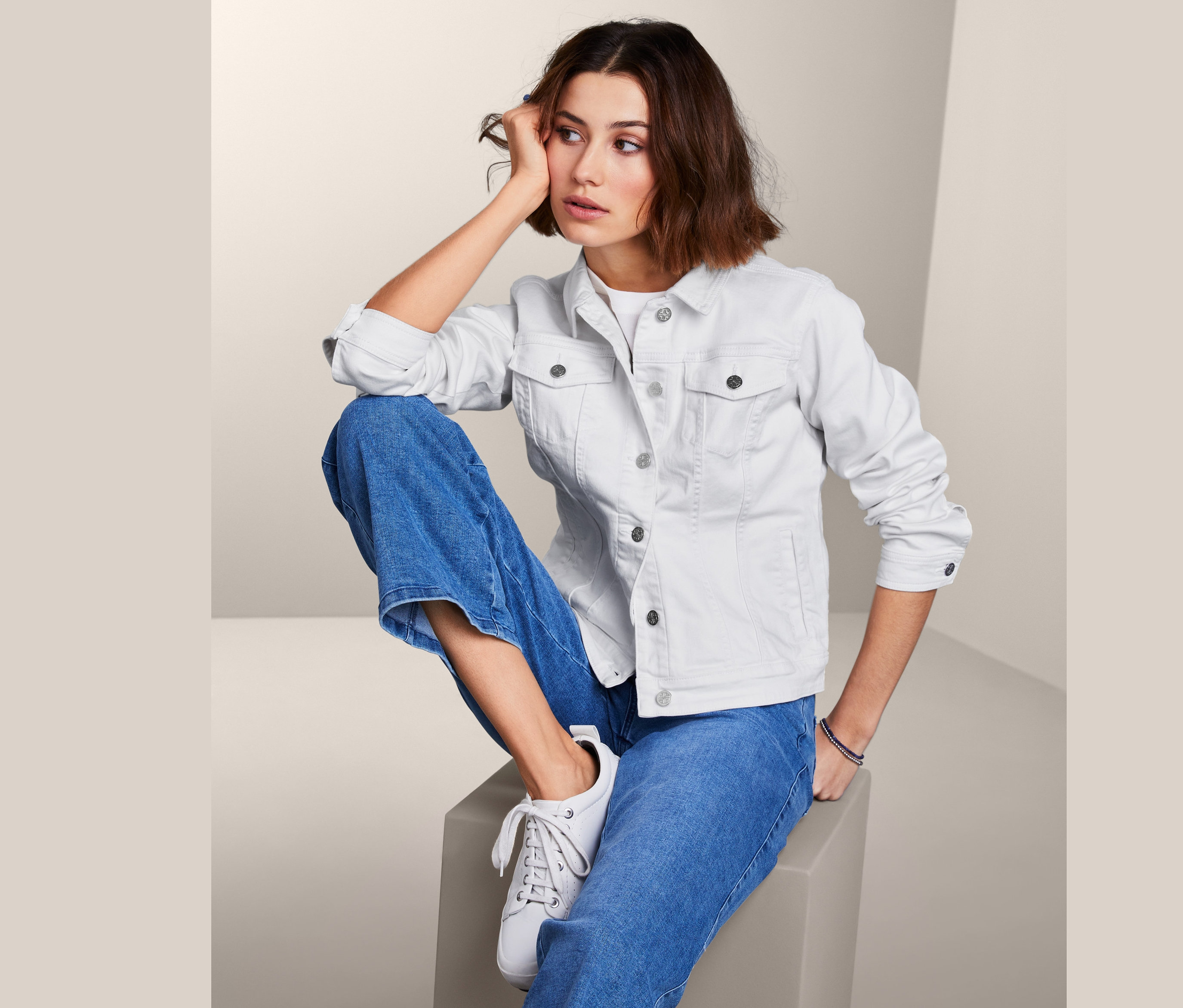 Kobieta siedzi i ma na sobie kurtkę dżinsową.