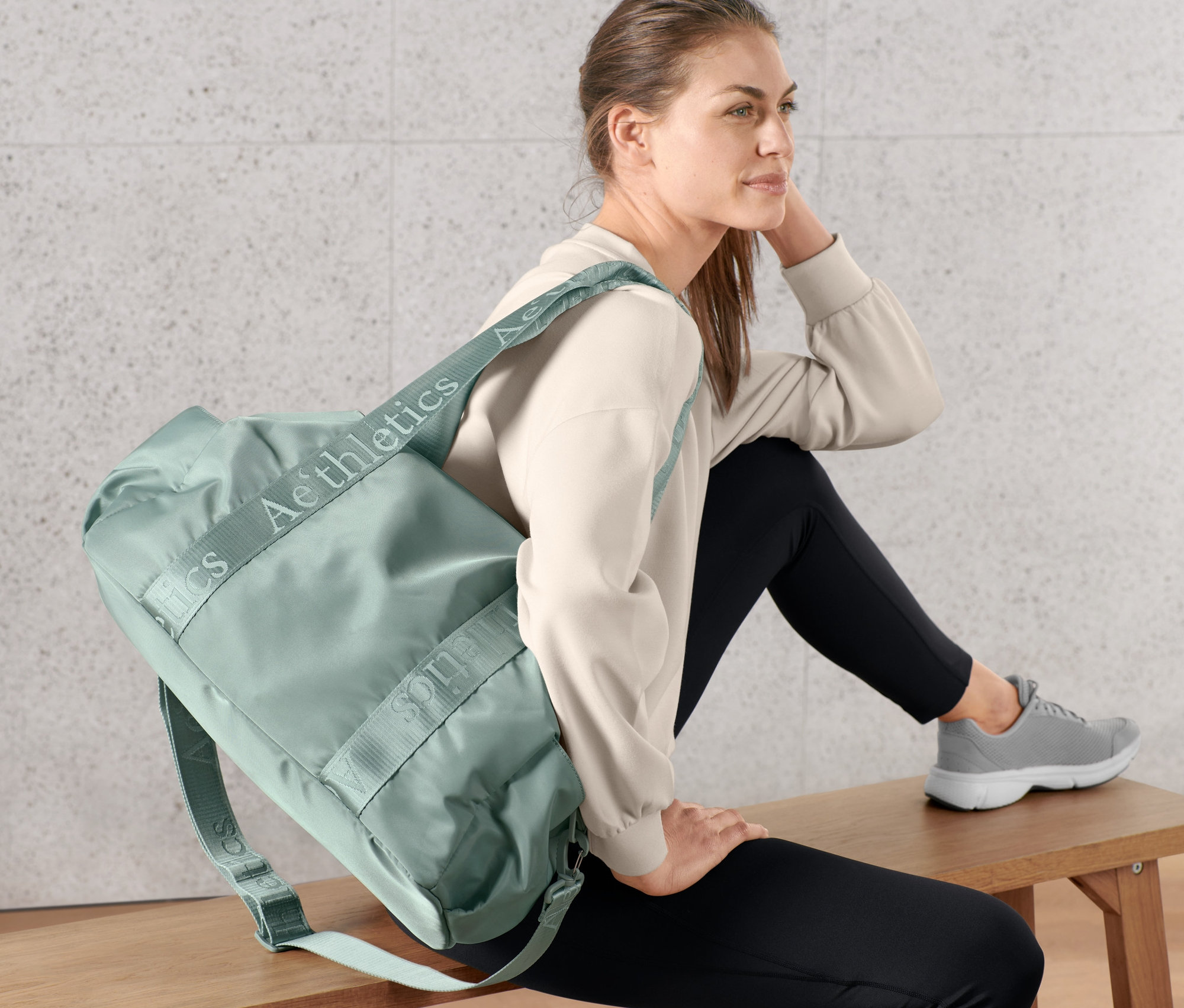 Kobieta siedzi na ławce z torbą sportową przewieszoną przez ramię.