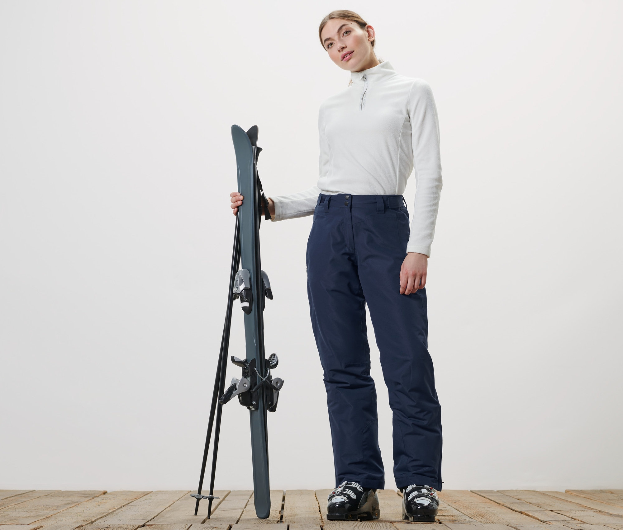 Kobieta trzyma narty i ma na sobie spodnie narciarskie.