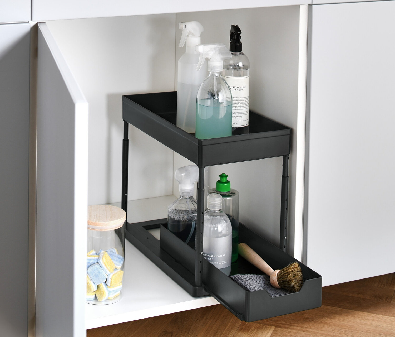 Otwarta biała szafka z wysuwaną szafką z regulacją wysokości, zawierającą środki czyszczące.