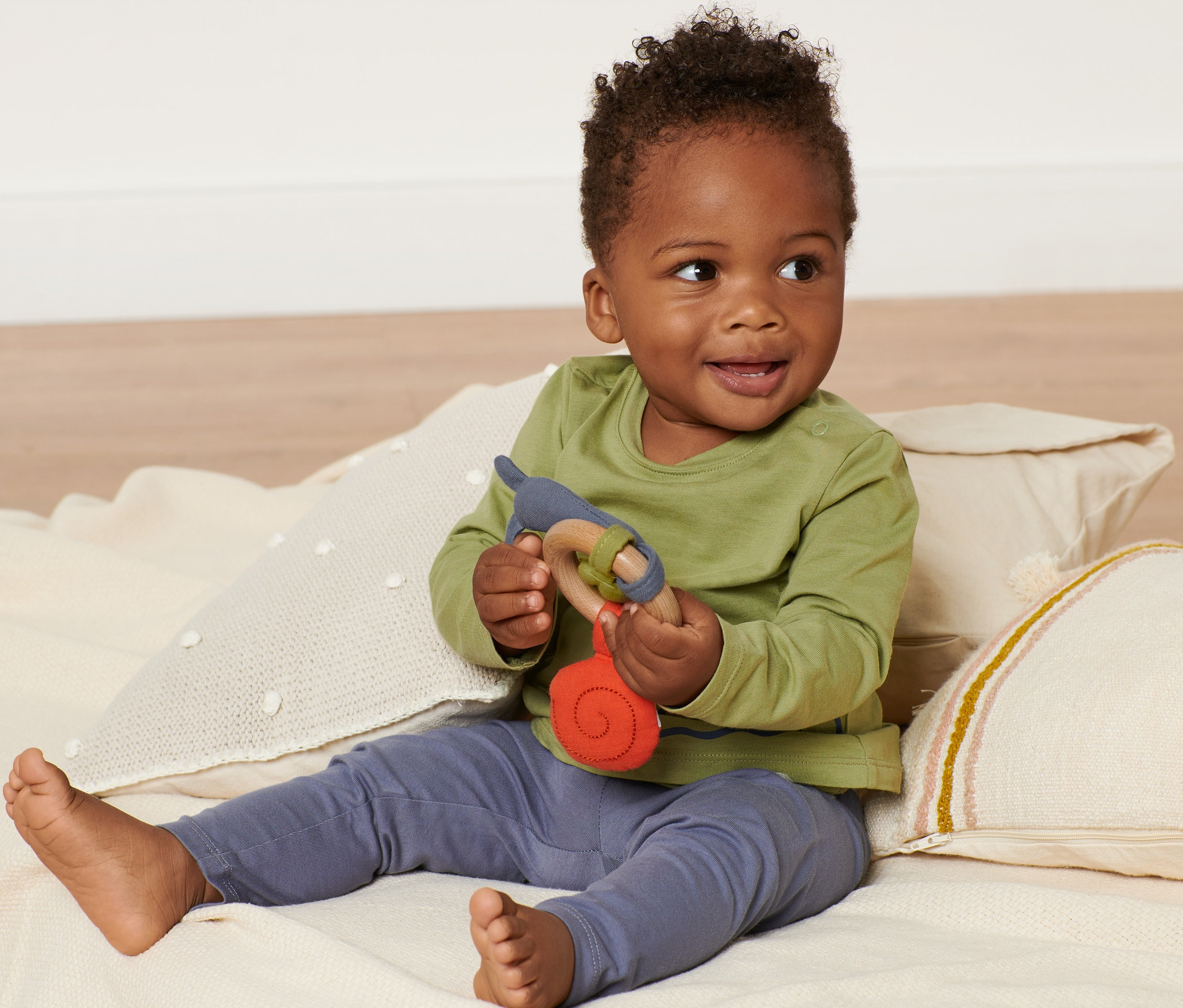 Uśmiechnięte dziecko siedzi na kocu i trzyma zabawkę dla niemowląt.