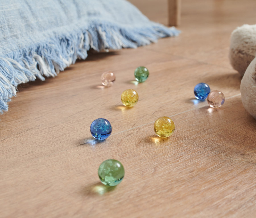 Świecące kulki w różnych kolorach leżą na podłodze obok pluszowego psa i niebieskiego koca.