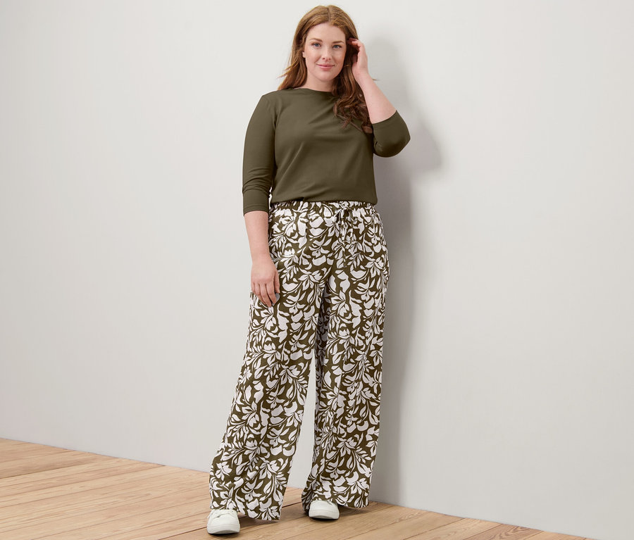 Kobieta pozuje w khaki bluzce z rękawem o długości 3/4 i wzorzystych spodniach na gumce.