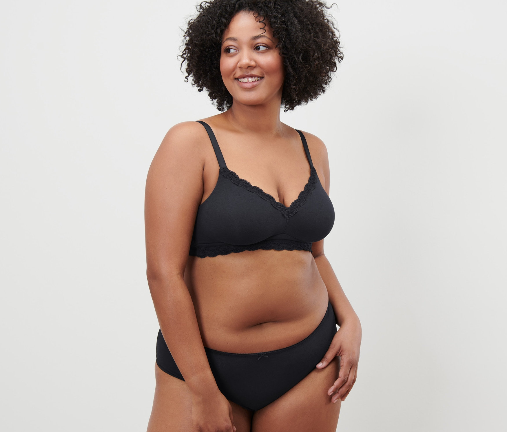 Kobieta z kręconymi włosami pozuje w czarnym miękkim biustonoszu.