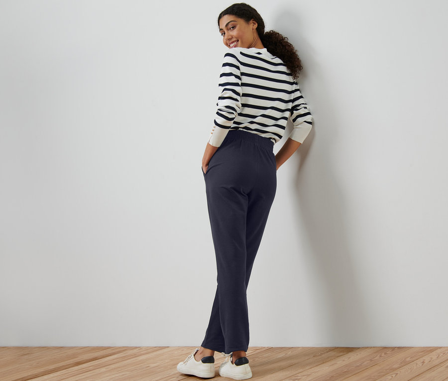 Kobieta stoi i pozuje w granatowych spodniach dresowych.