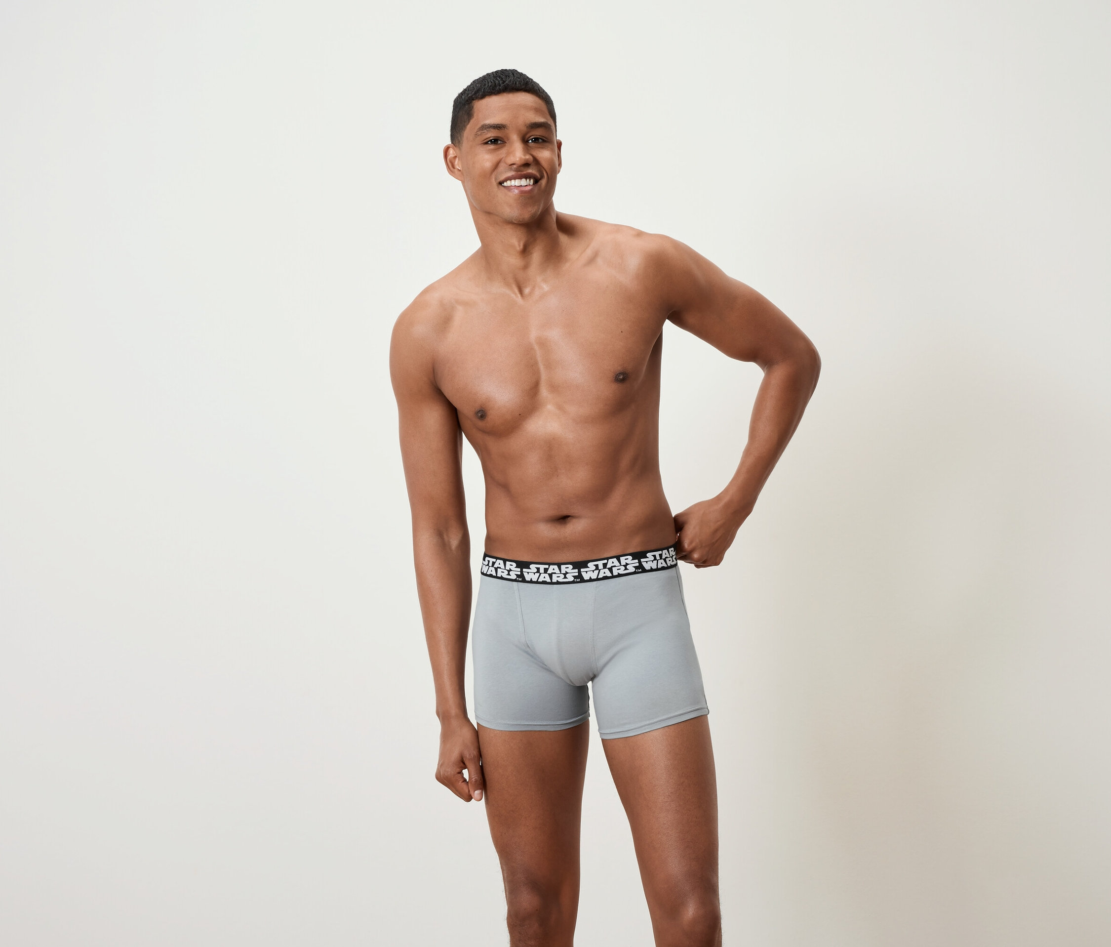 Uśmiechnięty mężczyzna pozuje bez koszulki, ubrany w szare bokserki marki Star Wars.