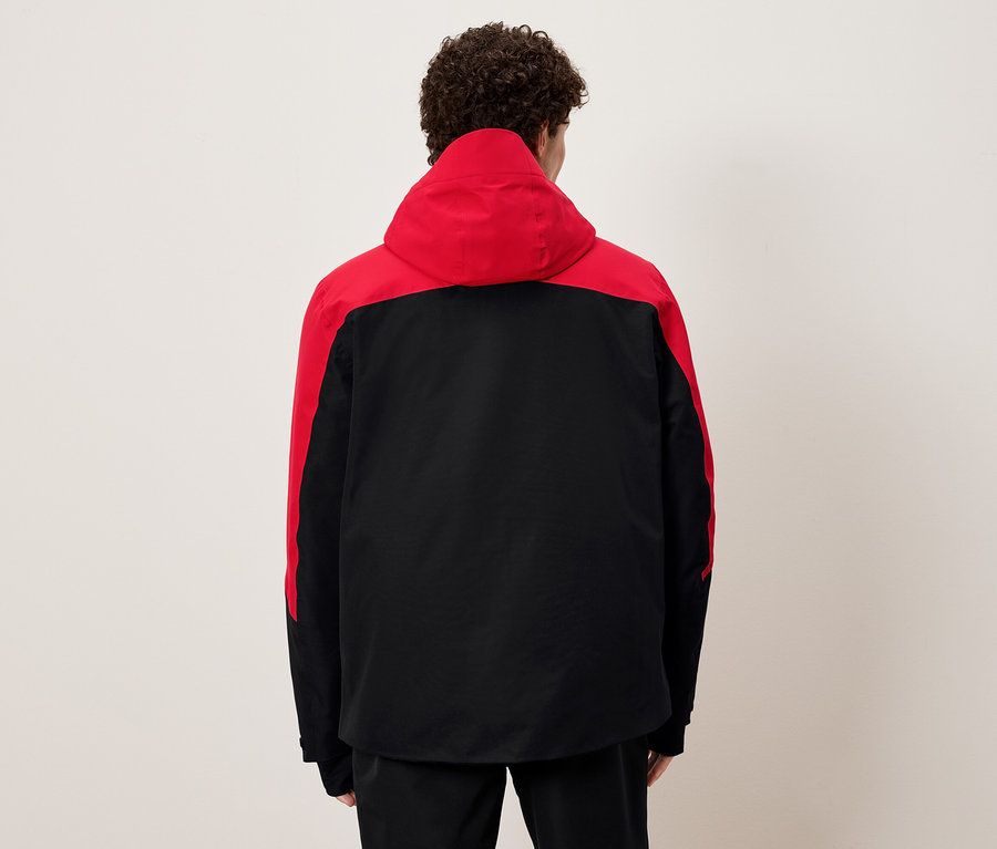 Mężczyzna tyłem do kamery ubrany w czarno-czerwoną kurtkę z kapturem.