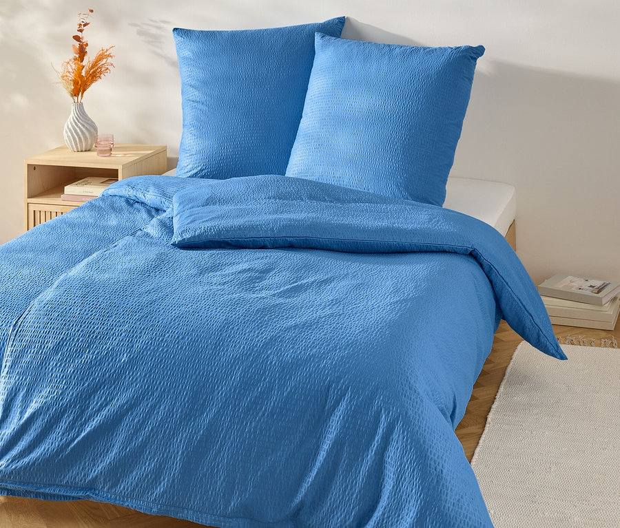 Niebieska pościel z kory w standardowym rozmiarze na łóżku z szafką nocną.