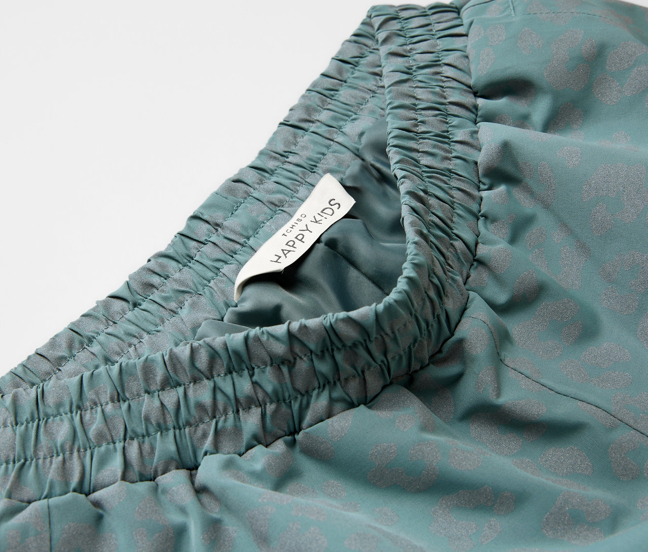 Zbliżenie na spodnie przeciwdeszczowe z elementami odblaskowymi, elastycznym pasem i metką Happy Kids.