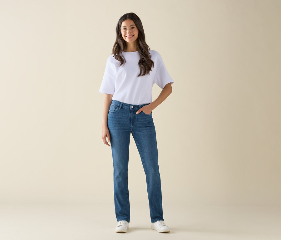 Kobieta stoi i pozuje w niebieskich jeansach, białym t-shircie i białych butach.