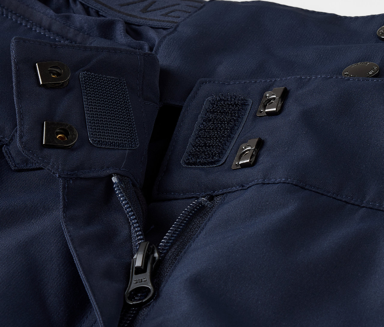 Szczegół granatowej kurtki z zamkiem błyskawicznym, rzepem i guzikami.