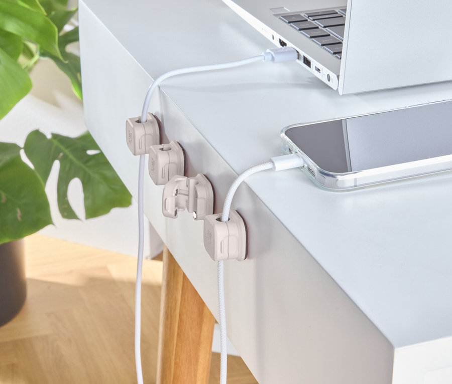 Srebrny laptop i telefon ładują się na białym biurku z drewnianymi uchwytami na kable.