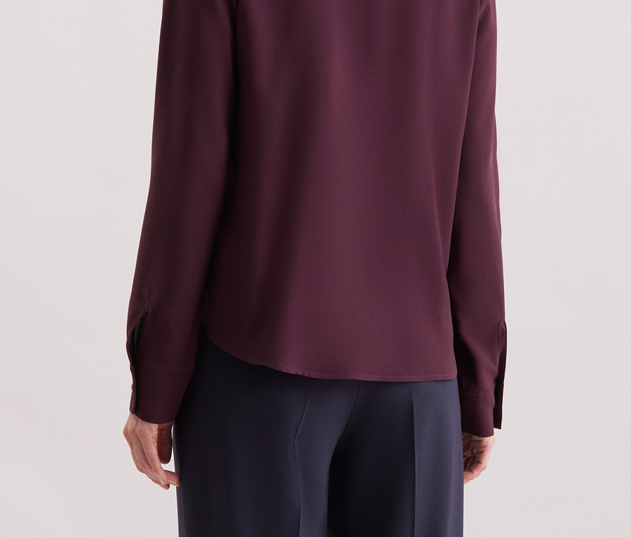 Z tyłu widoczna jest kobieta z blond włosami, ubrana w purpurową koszulę z długim rękawem.