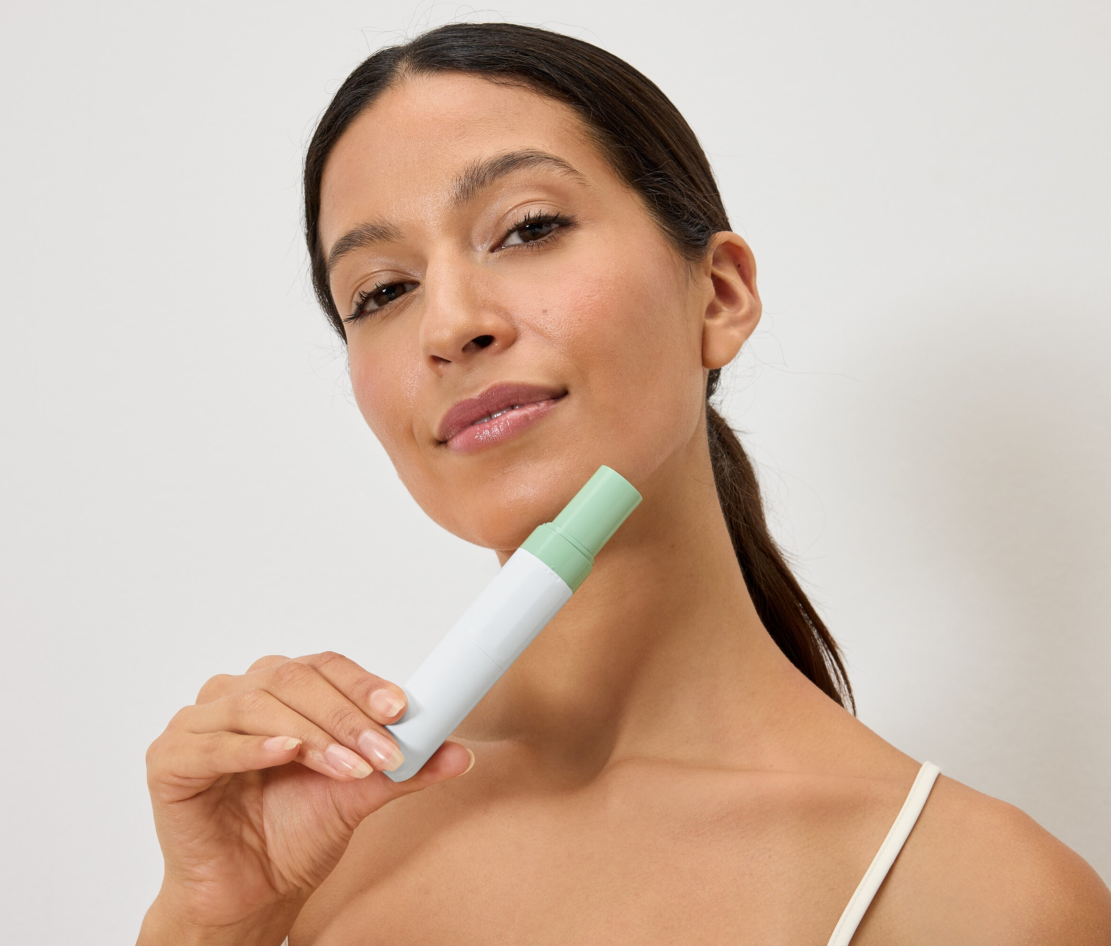 Kobieta trzyma biało-zieloną butelkę przed twarzą.