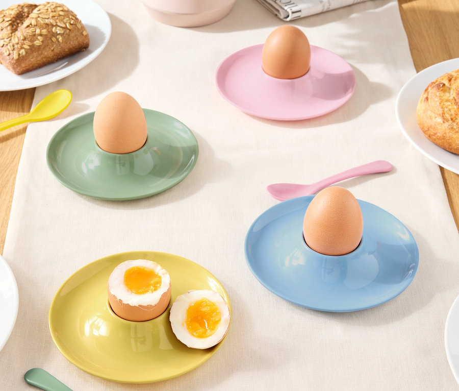 Kolorowe kieliszki do jajek z jajkami i łyżkami na obrusie.