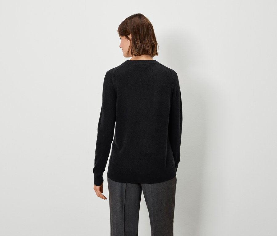 Kobieta w czarnym swetrze i szarych spodniach stoi tyłem do aparatu.