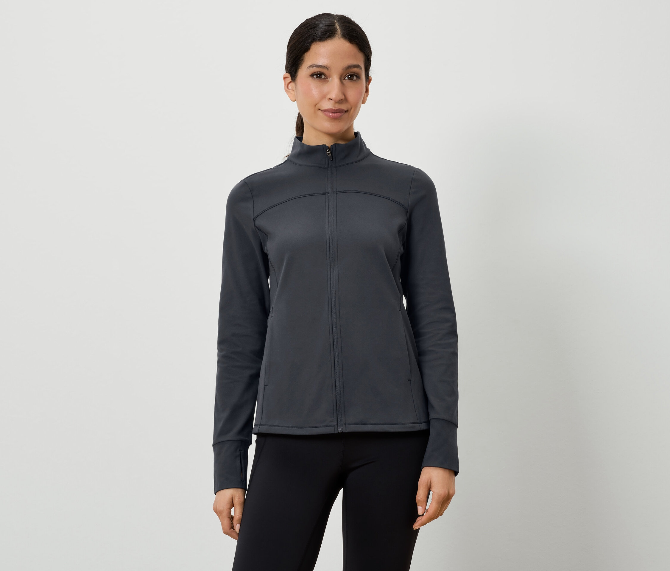 Kobieta ma na sobie ciemnoszarą kurtkę sportową i czarne legginsy.