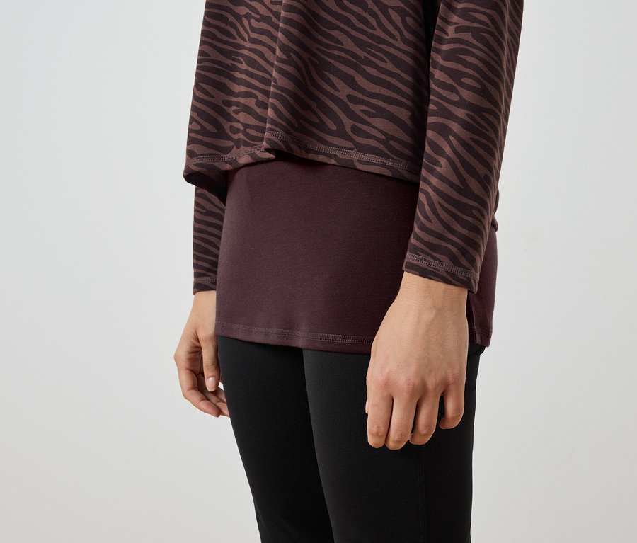 Zbliżenie na kobietę w brązowo-czarnej tunice w zebrę, bordowym topie i czarnych legginsach.