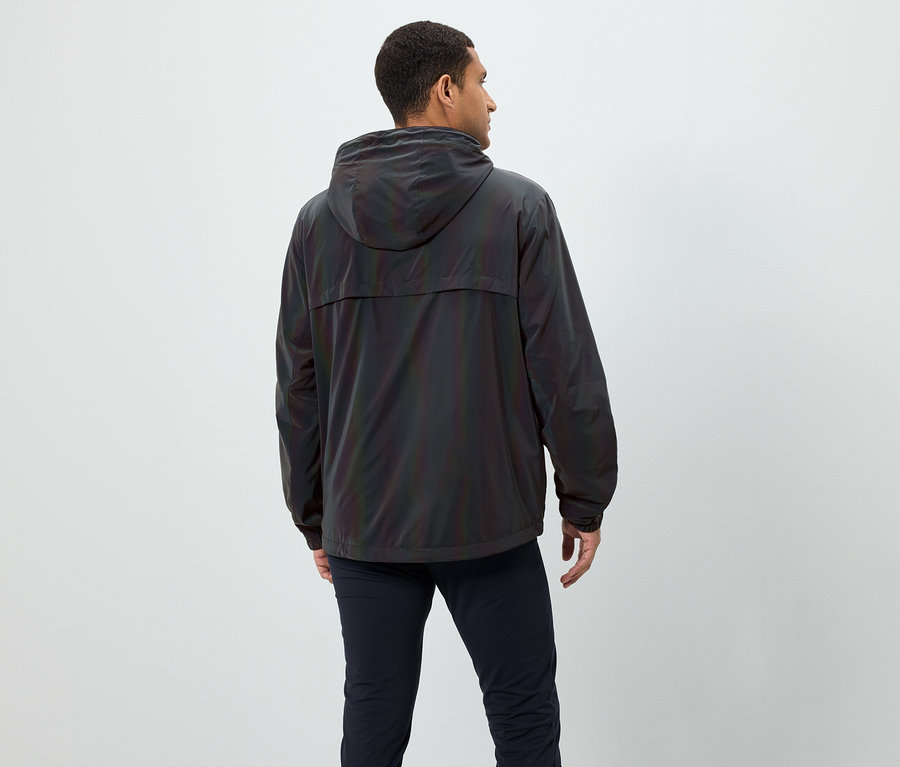 Mężczyzna od tyłu, ma na sobie opalizującą kurtkę z kapturem i granatowe spodnie.