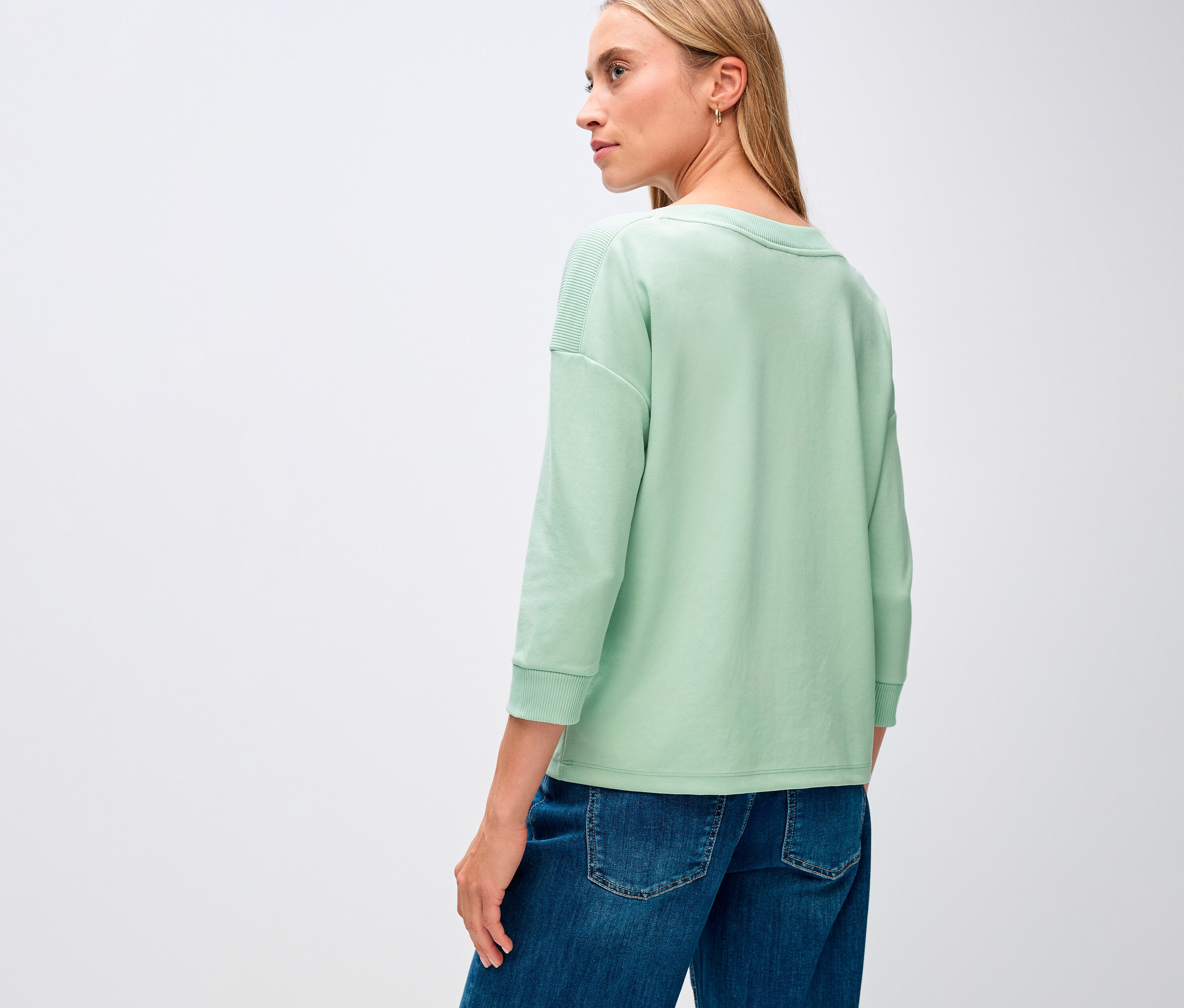 Kobieta ma na sobie szałwiową koszulkę z prążkowanymi detalami Street One.