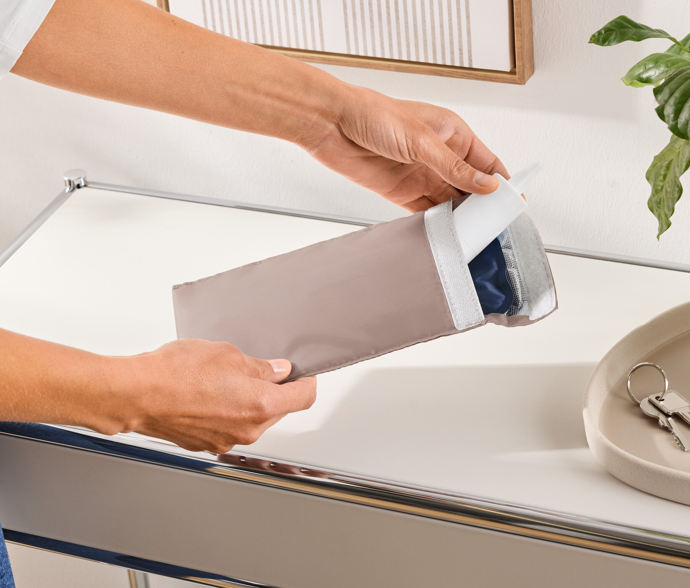 Osoba otwiera podłużny, beżowy pokrowiec ochronny zawierający niebieski produkt.