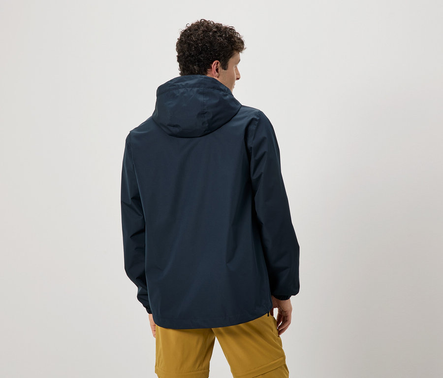 Widok z tyłu mężczyzny z kręconymi włosami w granatowej kurtce przeciwdeszczowej z kapturem i ochrowych spodniach.